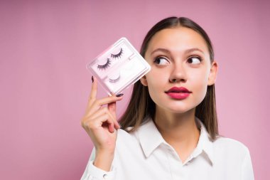 güzel kız pembe ruj, beyaz bir gömlek ile sahte kirpik elinde tutar.