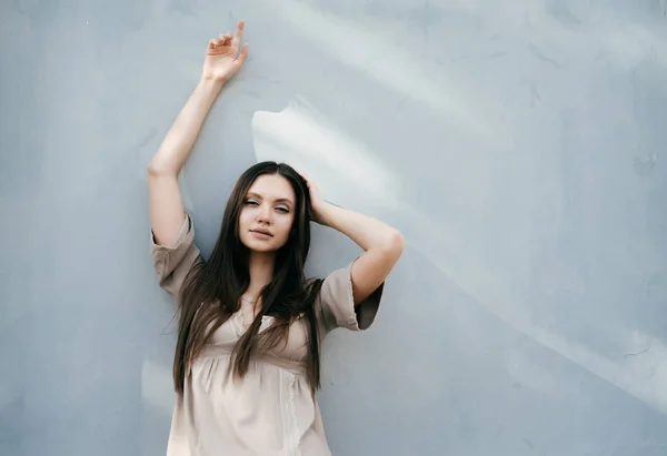 Sexy beautiful girl in a beige dress posing by a light wall — Stock Photo, Image