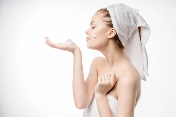 Bella ragazza con un asciugamano bianco sulla testa si prende cura del suo viso, applica schiuma detergente sul suo viso — Foto Stock