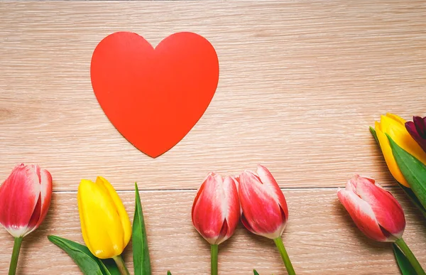 Sobre un suelo de madera yacen tulipanes amarillos y rojos, un dibujo de un corazón rojo —  Fotos de Stock