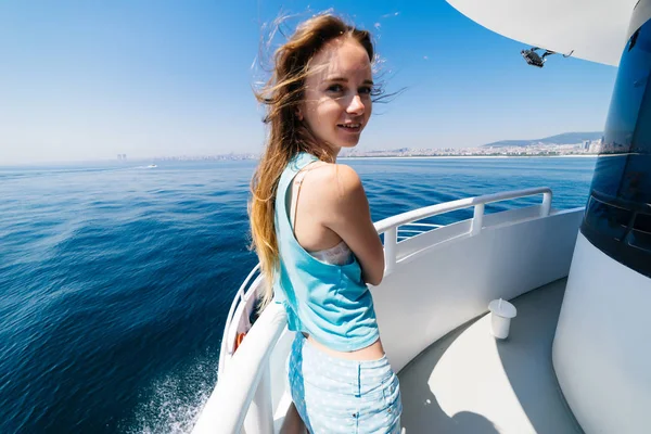 young girl in blue clothes is standing on a white yacht, around the blue sea, she is smiling