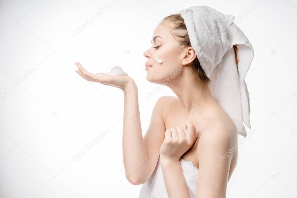 beautiful young girl with a white towel on her head looks after her face, applies cleansing foam on her face
