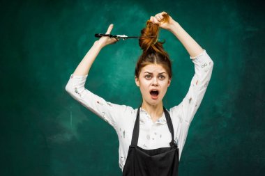 çılgın bir kız hakkında saçlarını makasla kesmeye ve yeşil bir arka plan üzerinde kameraya görünüyor