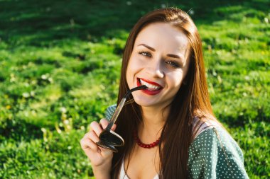 Gülümseyen kadın güneş gözlüğü, boşaltmak tutar. Gözlüklü. Yeşil çimenlerin üzerinde arka plan