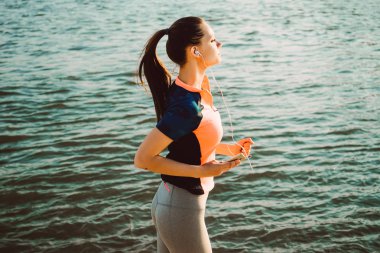 Spor takım elbiseli bir kız nehir kıyısında üzerinde çalışır ve kulaklıklar müzik dinler