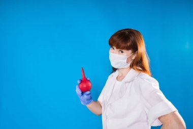 Kızıl saçlı hemşire maskeli lavman tutar ve izole kameraya benziyor