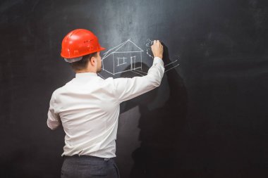 genç adam bir portakal inşaat kask içinde bir evi projesi tahtaya çizer.