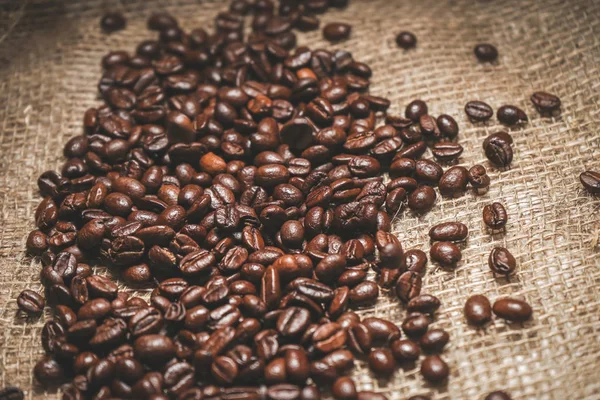 Kahverengi aromalı kahve çekirdekleri büyük bir yığın bir çanta üzerinde dağınık olduğunu — Stok fotoğraf