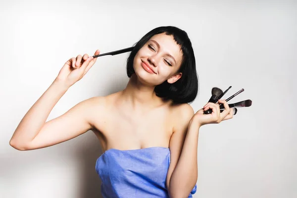 A menina após o chuveiro com cabelo curto preto está segurando as escovas de maquiagem em suas mãos e fechou os olhos — Fotografia de Stock