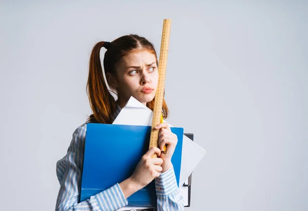 Ein trauriges Mädchen mit zwei Schwänzen hält ein Bündel Ordner mit Papieren und einem Lineal in der Hand und blickt traurig zur Seite — Stockfoto