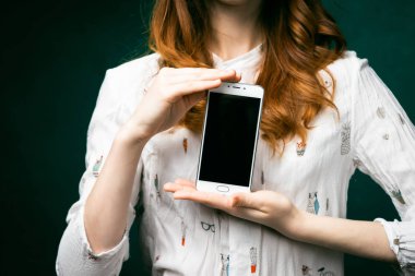 Kızıl saçlı bir kız telefonu gösterir