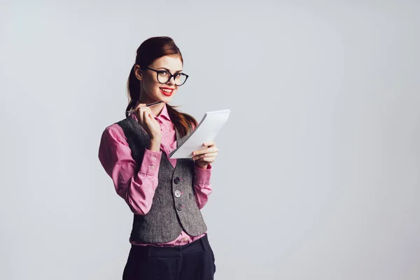 Junge Sekretärin mit Brille lächelt, während sie etwas ins Notizbuch schreibt — Stockfoto