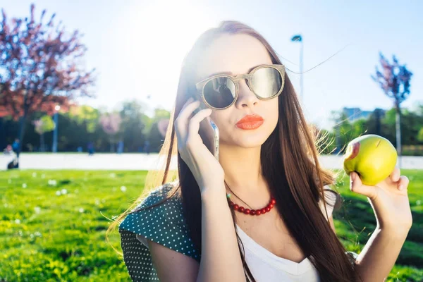 Angry woman holds mobile phone while sitting on a grass