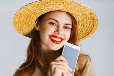 Kız şapka ve bir cep telefonu tutarak ve kameraya gülümseyen dudakları parlak ruj ile