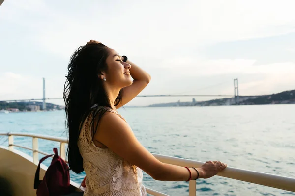 Молодая девушка путешественник расслабляется во время круиза по яхте, глядя на закат и океан, мост на заднем плане — стоковое фото