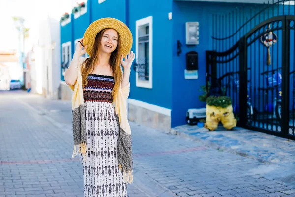 Señorita soleada con sombrero en la calle. la chica con un hermoso vestido se ríe. en el fondo una hermosa casa azul —  Fotos de Stock