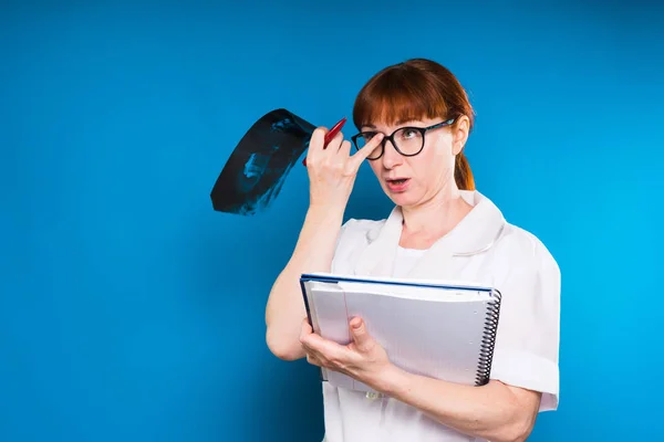 Krankenschwester in Brille hält Notizbuch und Röntgenbild, isoliert auf blauem Hintergrund — Stockfoto
