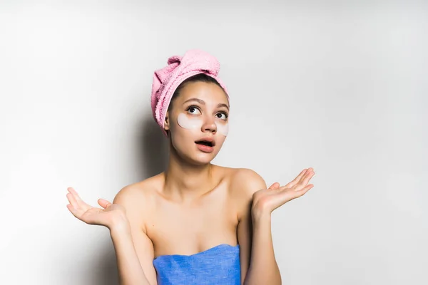 Девушка после душа с розовым полотенцем на голове и пятнами на лице удивлена чем-то и смотрит вверх — стоковое фото