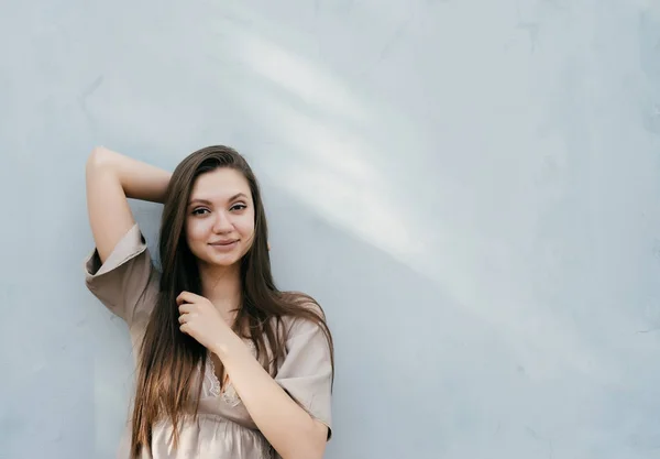 Όμορφη χαριτωμένο κορίτσι με μακριά μαλλιά στέκεται από τοίχο και χαριτωμένο χαμογελά στη φωτογραφική μηχανή — Φωτογραφία Αρχείου