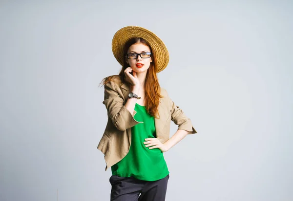 Menina em um chapéu com óculos e em uma jaqueta brilhante verde belamente se levanta e olha para a câmera, isolada em um fundo verde — Fotografia de Stock