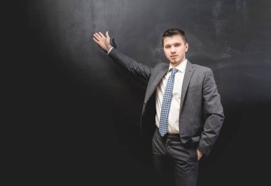 elbiseli genç adam blackboard standları ve eliyle tahtaya puan ve kameraya görünüyor