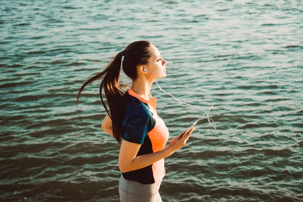 Een meisje in een sport-pak loopt langs de kade en luistert naar muziek op koptelefoon — Stockfoto