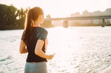 Spor uzun saçlı kız nehirde gün batımında, kulaklıklar müzik dinlemek çalışır