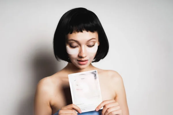 Krásná mladá dívka s černými vlasy vypadá po obličeji, drží masku na obličej — Stock fotografie