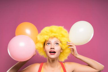 Sarı palyaço peruk başında komik bir kızla çok renkli balonlar görünüyor onun ellerinde havaya
