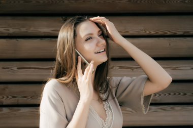 şık kız güler, güneşin telefonda konuşuyor, ahşap duvara yakın duruyor