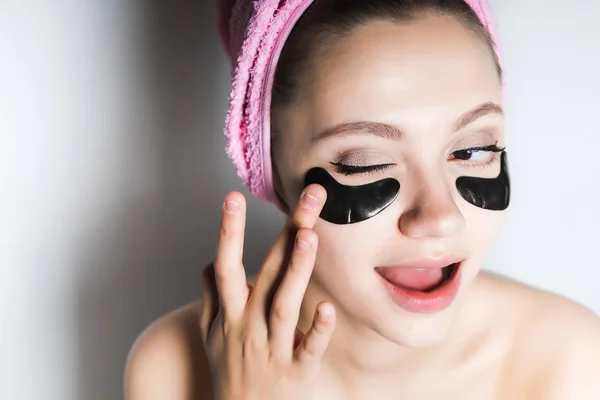 Κόλλες αστείο κορίτσι με καθαρό δέρμα, με μια ροζ πετσέτα στο κεφάλι της, κάτω από τα μάτια των patches μαύρο σιλικόνης — Φωτογραφία Αρχείου