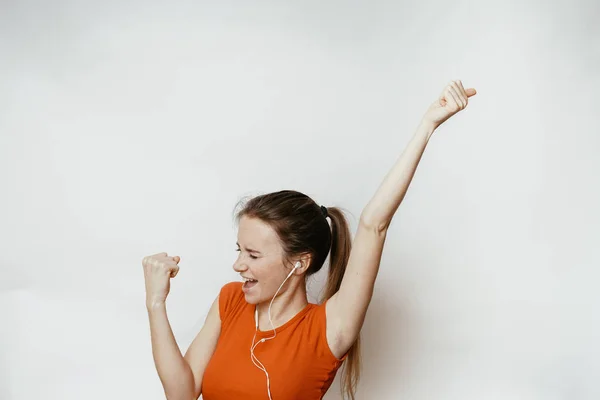 Счастливая женщина успеха выиграть возможность, обратно, наушники, в оранжевой футболке — стоковое фото