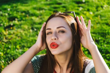 Güneş gözlüğü ile poz kadın yüzünü kapat, parkta yeşil çimenlerin üzerinde oturur