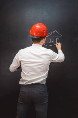 genç erkek inşaat Builder'da, beyaz gömlek, turuncu koruyucu kask tebeşir ile ev çizer