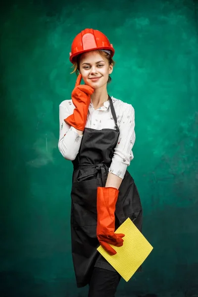 Uma menina sorridente em um capacete de proteção laranja e luvas de borracha segura um pano amarelo para limpeza — Fotografia de Stock