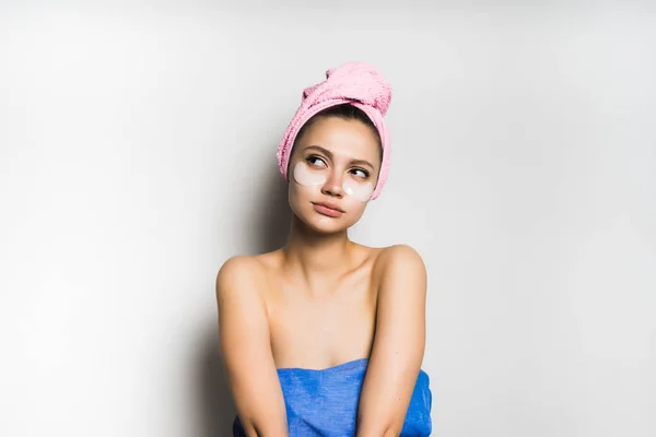 Giovane ragazza con un asciugamano rosa sulla testa, con macchie di silicone sotto gli occhi guardando pensieroso — Foto Stock