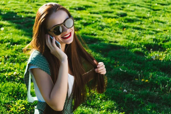 Woman talking with mobile,speaking,smiling.Girl in sunglasses,sits on the green grass in the park — Stock Photo, Image