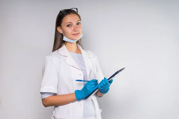 Hermosa joven médico en bata médica blanca sostiene portátil, mira a la cámara — Foto de Stock