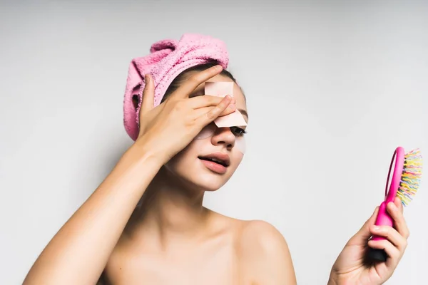 Όμορφη κοπέλα με μια ροζ πετσέτα στο κεφάλι της καθαρίζει το πρόσωπο, κρατά στα χέρια της ένα ροζ χτένα — Φωτογραφία Αρχείου