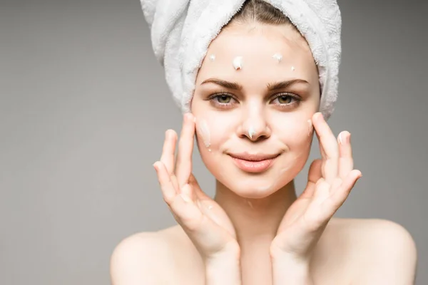 Charmante jeune fille avec une serviette blanche sur la tête s'occupe de son visage, applique de la crème, sourit — Photo