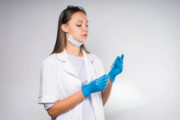 Giovane donna sicura di sé medico in vestaglia medica bianca, indossando guanti di silicone blu con una siringa — Foto Stock