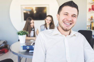 mutlu 2 kız ofiste bir proje üzerinde birlikte gülüyor, arkasından bir gömlek başarılı genç adam