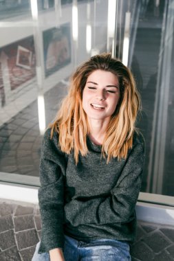 bir cam duvara oturan kalın saçlı güzel kız gülerek