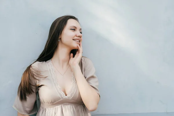 Attraktivt leende flicka modell med långt hår poserar vid en ljus vägg — Stockfoto