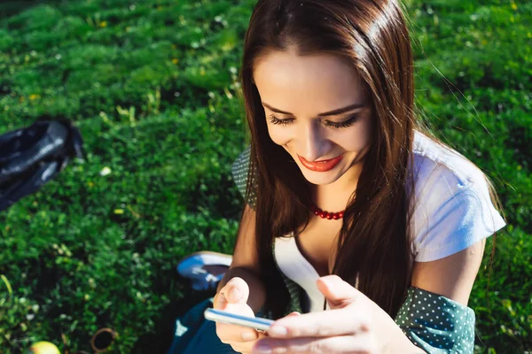 Cep telefonu, SMS, Park, yeşil çimenlerin üzerinde oturan kız sohbet gülümseyen