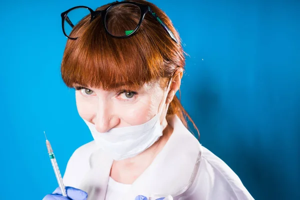Adulto esperto medico donna dai capelli rossi in maschera medica protettiva bianca sulla siringa tenuta in faccia, guardando la fotocamera — Foto Stock