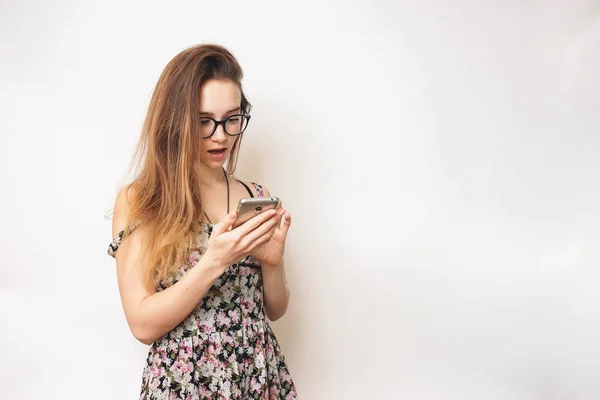 Chica joven de pelo largo con gafas mira su teléfono inteligente con sorpresa — Foto de Stock