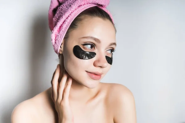 Roztomilá dívka s čistou pleť vypadá po tváři, na hlavu růžový ručník, pod její oči černé silikonové náplasti — Stock fotografie