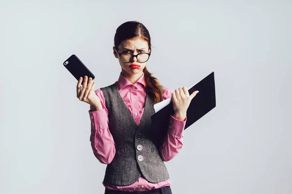 Das traurige junge rothaarige Mädchen mit Brille und rosa Hemd hält ein Smartphone und Dokumente in der Hand. — Stockfoto