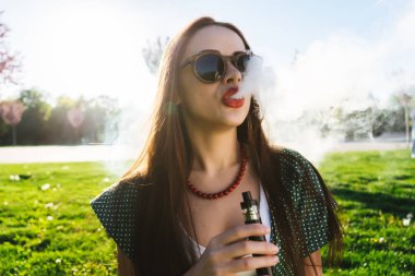 Mutlu moda gülümseyen kadın güneş gözlüğü vape Street, duman Sigara